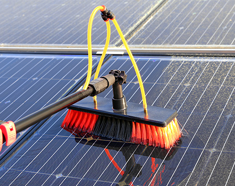 a pressure washer with a brush attachment cleaning a roof of solar panels