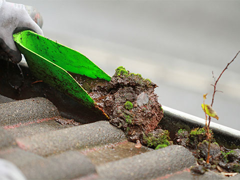 a person scraping dirt, moss and grime out of a gutter on a roof