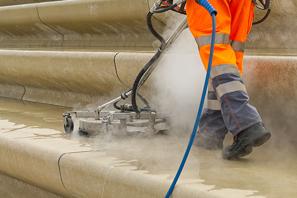 a person wearing hi-vis overalls using a power washer to wash steps on a pavement 